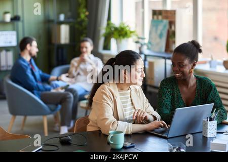 Zwei junge kreative Mitarbeiter diskutieren Ideen, während sie vor dem Laptop am Schreibtisch sitzen und an einer neuen Website oder einem anderen Projekt arbeiten Stockfoto