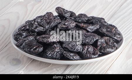 Saftig leckere Pflaumen auf einem weißen Teller auf einem alten weißen Holztisch. Draufsicht. Stockfoto