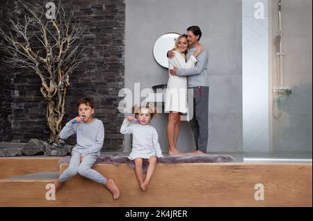 Wunderschöne kaukasische Familie, die morgens wascht und Zähne putzt. Glückliche Mama, Papa und Kinder im Badezimmer im Hotelzimmer oder zu Hause Stockfoto