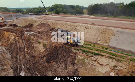 Langer Raupenbagger bewegt die Erde auf einer Baustelle und gräbt die Gräben für die Verlegung von Rohrleitungen. Warschau, Polen. . Hochwertige Fotos Stockfoto