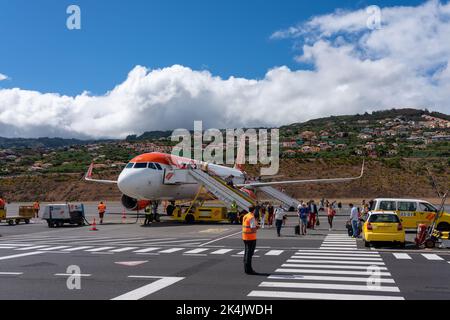 Madeira Island, Portugal - 2022, August 26. - Passanten, die aus einem Easyjet-Flugzeug auf dem Cristiano Ronaldo International Airport mit Häusern i laufen Stockfoto