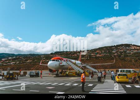 Madeira Island, Portugal - 2022, August 26. - Passanten, die aus einem Easyjet-Flugzeug auf dem Cristiano Ronaldo International Airport mit Häusern i laufen Stockfoto