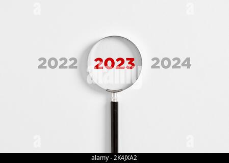 Die Lupe vergrößert das Jahr 2023 zwischen den Jahren 2022 und 2024 auf weißem Hintergrund. Konzentration auf das Jahr 2023 oder Analyse für den Businessplan Stockfoto