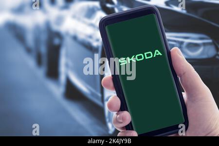 Galicia, Spanien; januar 09 2021: Hand hält ein Smartphone mit neuem SKODA-Logo auf dem Bildschirm. Verschwommene Autos im Hintergrund Stockfoto