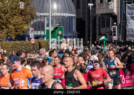 Lustige Läufer, die beim TCS London Marathon 2022 auf der Tower Hill Road, City of London, Großbritannien, am Tower Gateway und jubelnden Publikum vorbeilaufen Stockfoto