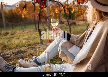 Frau, die im Weinberg sitzt und Weißwein trinkt. Entspannung im Herbst Weingut nach der Weinlese Stockfoto