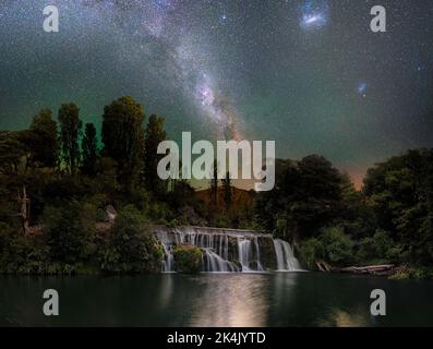 Die schöne Aussicht auf einen Wasserfall und grüne Vegetation mit Milchstraße im Hintergrund. Neuseeland. Stockfoto