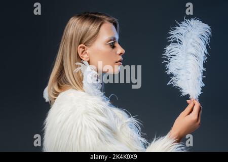 Seitenansicht der blonden Frau mit Winter Make-up Blick auf Feder isoliert auf blau, Stock Bild Stockfoto