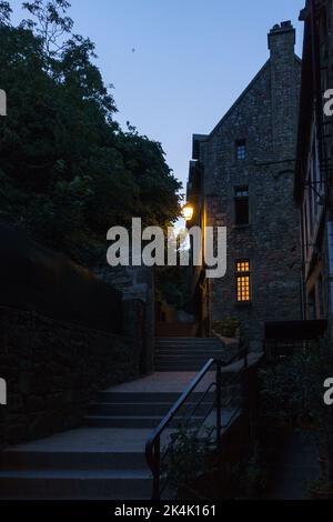 Typischer Blick auf die Straße bei Nacht mit Lampe, die über Treppen am Le Mont Saint Michel, Normandie, Frankreich hängt Stockfoto
