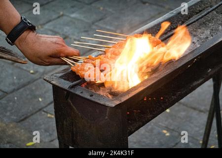 Malaysia, 10. Juli 2022 - Hühnerspieße, die auf einem Nachtmarkt am offenen Feuer gekocht werden. Stockfoto