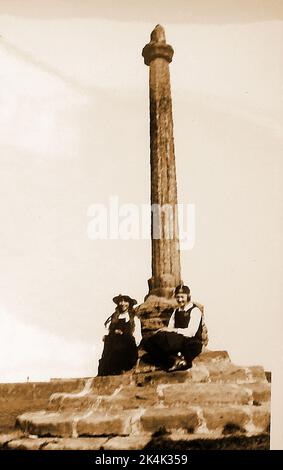 Eine sehr frühe Momentaufnahme von zwei Schulmädchen in Uniform, die auf den Stufen des alten Marktkreuzes in der Nähe von Whitby Abbey auf der Ebene der Abtei (Ebene der Abtei) sitzen Stockfoto
