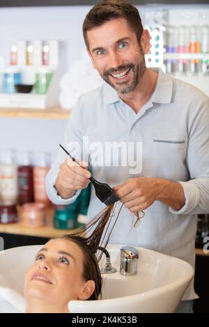 Männlicher Friseur, der die Haare der Frau über dem Waschbecken verfärbt Stockfoto