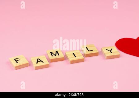 Die Wortfamilie besteht aus Holzbuchstaben und einem halben roten Herzen auf einem rosa Hintergrund. Familientag. Stockfoto