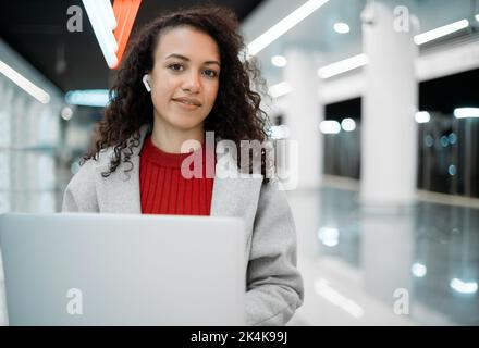 Lächelnde Bloggerin mit einem Laptop auf einer Bank in der U-Bahn. Stockfoto