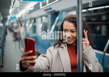 Glückliche junge Frau, die in der U-Bahn steht und einen Videoanruf entgegennimmt. Stockfoto