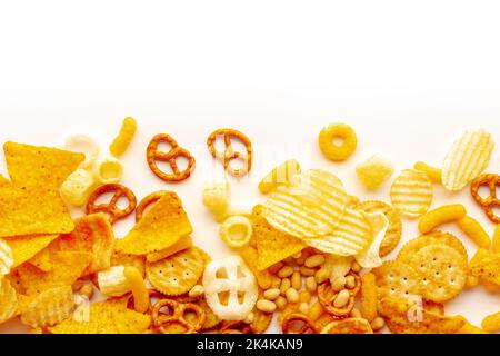 Salzige Snacks auf weißem Hintergrund mit Platz zum Kopieren. Kartoffel- und Tortilla-Chips, Salzkräcker und andere Vorspeisen, von oben geschossen Stockfoto