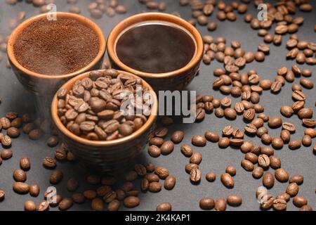 Frisch gemahlener und gebrühter schwarzer Kaffee auf schwarzem Hintergrund, drei Tassen mit gedämpftem Kaffee. Stockfoto