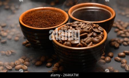 Tassen Kaffee unter ausgewählten und kalibrierten Arabica-Kaffeebohnen, verteilt auf schwarzem Hintergrund, drei aromatische Tassen Kaffee in einem Paar. Stockfoto