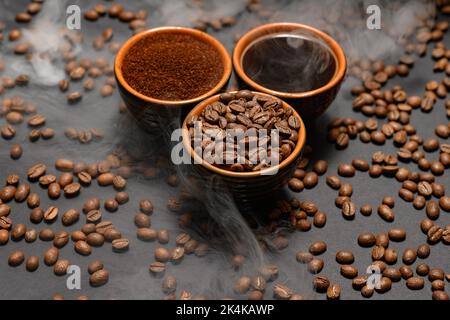 Kaffeetassen und geröstete Kaffeebohnen auf schwarzem Hintergrund in einem Paar, schwarze Kaffeebohnen, gemahlen und frisch gebrüht. Stockfoto