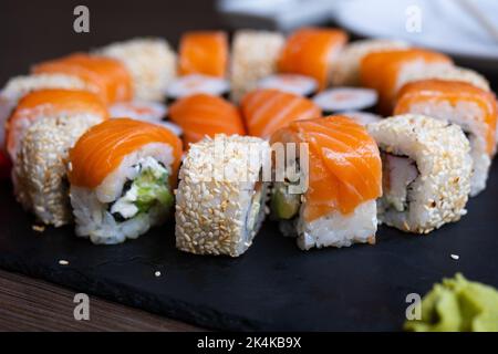 Köstliche, frische Sushi-Rolle auf einem schwarzen Brett. Sushi-Rolle mit Reis, Frischkäsen, rotem Fisch, Lachs. Sushi-Menü. Japanische Küche, Restaurant. Seafoo Stockfoto