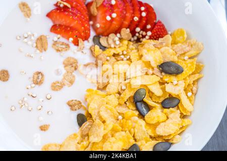 Joghurt-Schüssel mit frisch geschnittenen Erdbeeren und trockenen Maisflocken. Traditionelles Frühstückskonzept mit Cornflakes. Gesunde Ernährung Konzept. Lebensmittel und Gesundheit Stockfoto