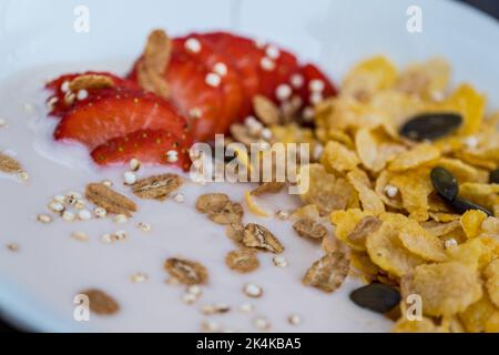 Joghurt-Schüssel mit frisch geschnittenen Erdbeeren und trockenen Maisflocken. Traditionelles Frühstückskonzept mit Cornflakes. Gesunde Ernährung Konzept. Lebensmittel und Gesundheit Stockfoto