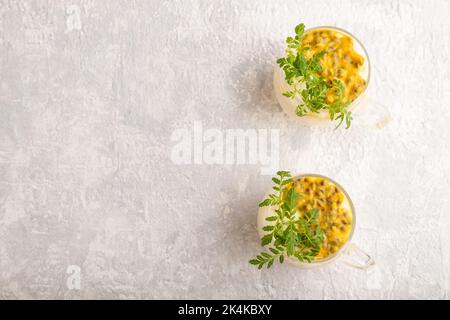Joghurt mit Passionsfrucht und Ringelblume Microgreen in Glas auf grauem Betongrund. Draufsicht, flach liegend, Kopierbereich. Stockfoto