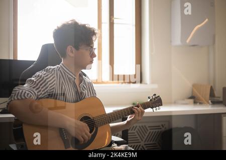 Männlicher Teenager singt Lied spielt akustische Gitarre und liest Text auf dem Smartphone-Anwendungsbildschirm Stockfoto