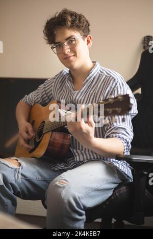 Männlicher Teenager singt Lied spielt akustische Gitarre und liest Text auf dem Smartphone-Anwendungsbildschirm Stockfoto