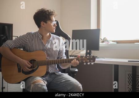 Männlicher Teenager singt Lied spielt akustische Gitarre und liest Text auf dem Smartphone-Anwendungsbildschirm Stockfoto