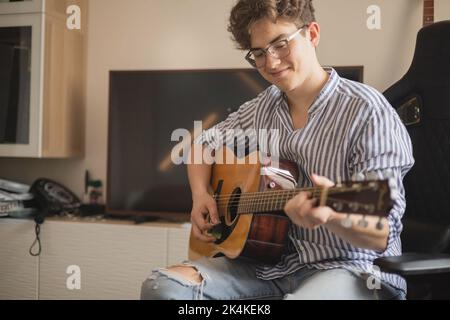 Männlicher Teenager singt Lied spielt akustische Gitarre und liest Text auf dem Smartphone-Anwendungsbildschirm Stockfoto