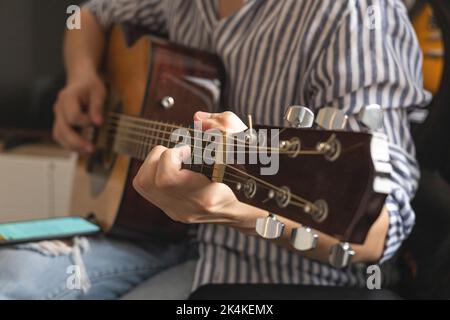 Männlicher Teenager singt Lied spielt akustische Gitarre und liest Text auf dem Smartphone-Anwendungsbildschirm Stockfoto