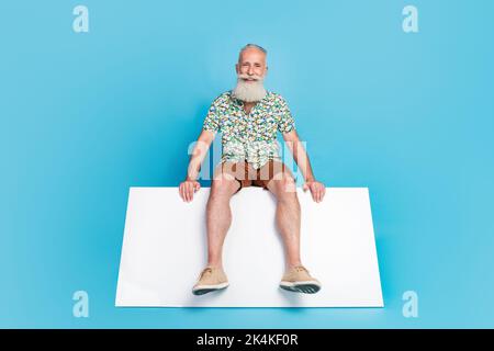 Foto in voller Größe von fröhlichen positiven Mann sitzen leeren Raum Podium isoliert auf blauem Hintergrund Stockfoto