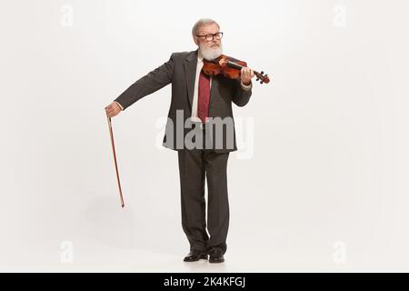 Älterer Mann, Musiker, der Geige spielt, isoliert über weißem Studiohintergrund. Konzept von Retro, Vintage-Mode, Kunst, Musik Stockfoto