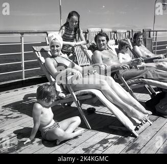 1960er Jahre, historisch, fröhlich, eine Familie, die sich auf Liegestühlen auf dem Deck des norweigisch-amerikanischen Kreuzfahrtschiffs MS Sagafjord, einem luxuriösen Kreuzfahrtschiff der damaligen Zeit, entspannt. Stockfoto