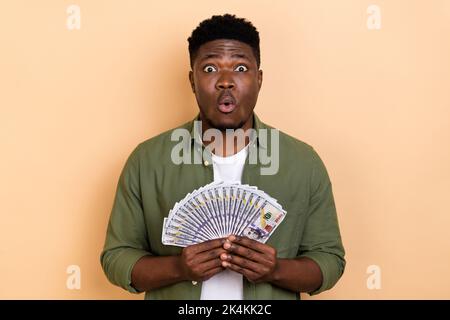 Foto von beeindruckt jungen Brunet Kerl halten Geld tragen lässige Tuch isoliert auf beige Farbe Hintergrund Stockfoto
