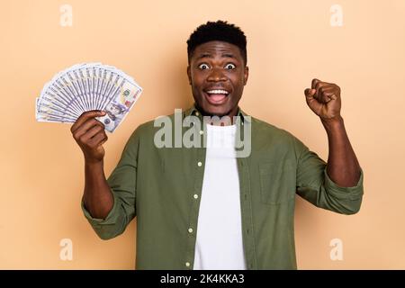 Foto von coolen jungen Brunet Kerl halten Geld brüllen tragen khaki Shirt isoliert auf beige Farbe Hintergrund Stockfoto