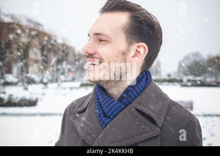 Porträt eines jungen, hübschen Mannes mit lächelndem Bart, der im Winterschnee lacht Stockfoto
