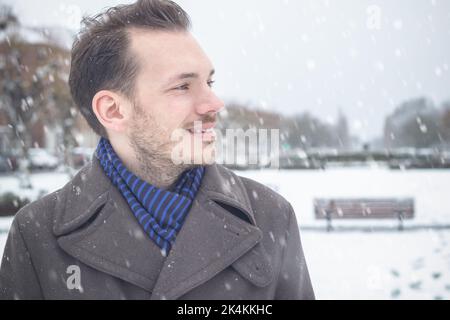 Porträt eines jungen, hübschen Mannes mit lächelndem Bart, der im Winterschnee lacht Stockfoto