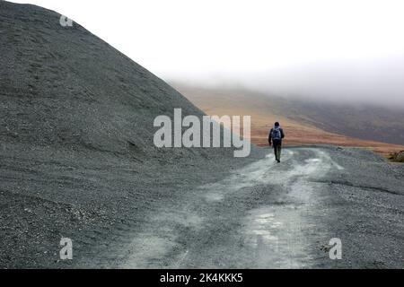 Der einträchtige Mann, der am Honister Slate Quarry vorbei an Verderbhaufen vorbeigeht, führt zu den Wainwright „Grey Knotts“ im Lake District National Park, Cumbria, England. Stockfoto