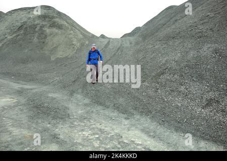 Der einträchtige Mann, der am Honister Slate Quarry vorbei an Verderbhaufen vorbeigeht, führt zu den Wainwright „Grey Knotts“ im Lake District National Park, Cumbria, England. Stockfoto