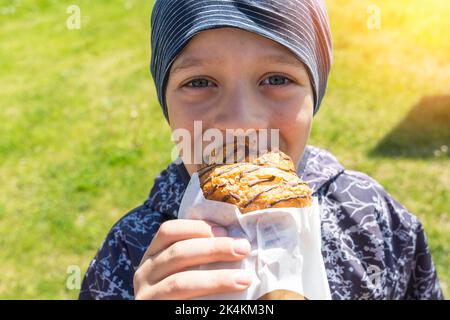 Ein fröhlicher, fröhlicher Junge isst auf der Straße ein Brötchen Stockfoto