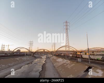 Eine Drohne, die bei Sonnenuntergang im Los Angeles River über der 6. Street Bridge fliegt Stockfoto