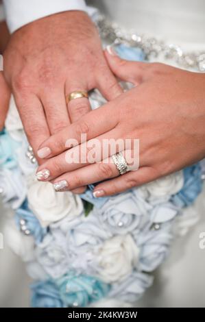 Braut und Bräutigam überreichen Hochzeitsblumen mit ihren Eheringen Stockfoto