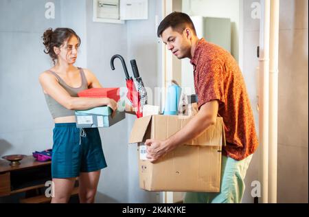 Ein junges Paar zieht in ihre neue Wohnung. Sie sind von Kisten, Paketen und anderen Dingen umgeben. Stockfoto