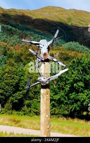 Zwei gebrauchte Drohnen, die an ein Warnschild angebracht sind, das darauf hinweist, dass keine Drohne auf dem Glenfinnan Estate in den schottischen Highlands in Glenfinnan, Schottland, Großbritannien, fliegt. Stockfoto