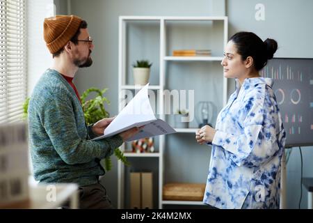 Junge, seriöse Geschäftsmänner, die manuell mit einer Kollegin in eleganter Casualwear sprechen und ihre Fragen vor dem Seminar beantworten Stockfoto