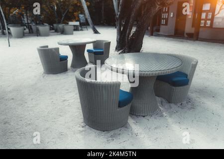 Ein Weitwinkelblick mit einem selektiven Fokus auf die Gruppe leerer Outdoor-Wicker-Cafétische auf dem Korallenstrand einer Straßenbar oder eines Hotelrestaurants von A Stockfoto