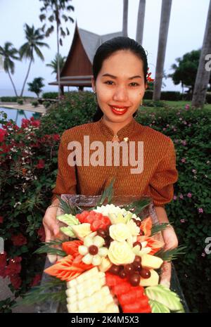Thailand. Hua Hin. Chiva Som International Health Resort. Junge Thailänderin hält Tablett mit traditionellen geschnitzten Früchten. Stockfoto