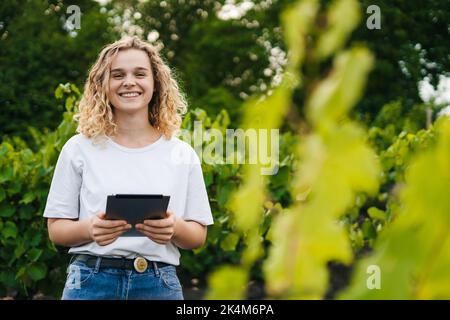 Porträt einer Farmerin mit digitalem Tablet, die auf einem landwirtschaftlichen Weinbergfeld steht. Intelligente Landwirtschaft und digitale Landwirtschaft. Futuristisch Stockfoto